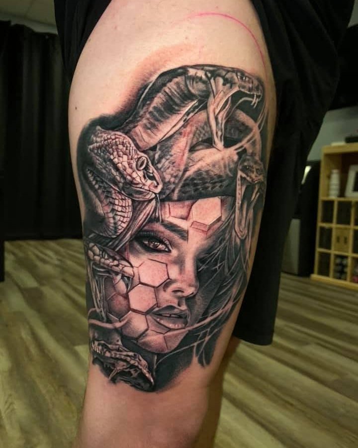 Black and grey Medusa portrait tattoo with snakes and geometric shading on the upper arm